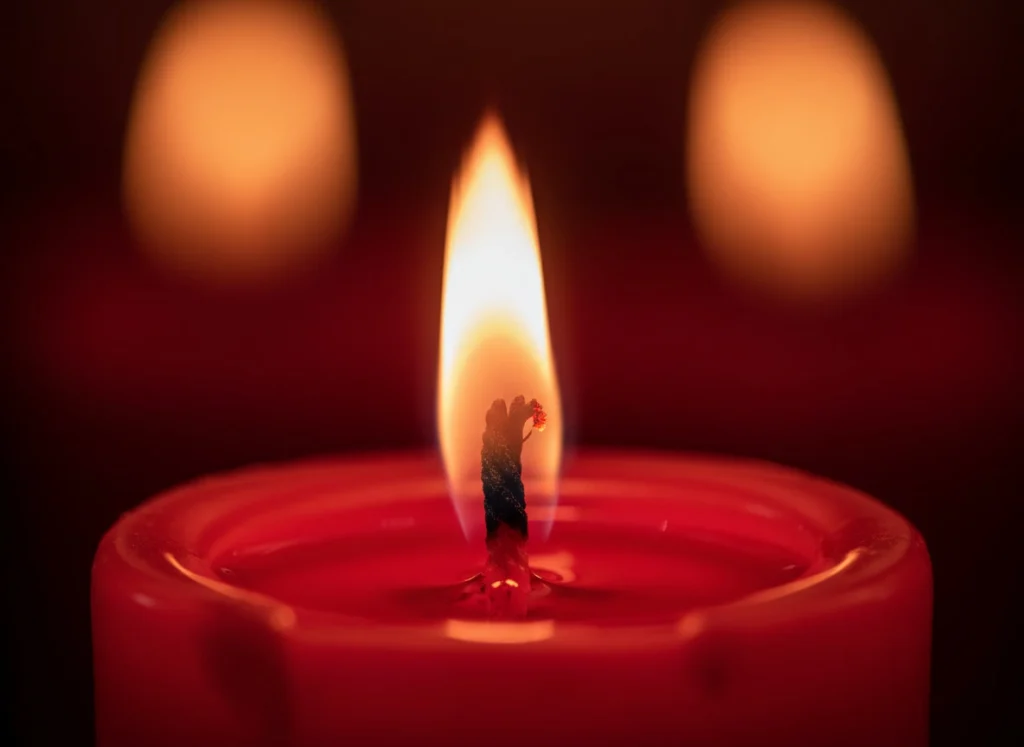 Llama de vela roja en primer plano, cera carmesí y halo cálido